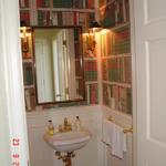 A guest half bath with specialty wallpaper (books on shelves)